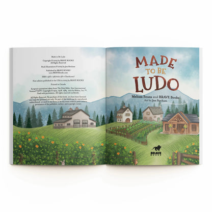 Open book showing a landscape illustration with houses and trees, and 'Made to be Ludo' text.